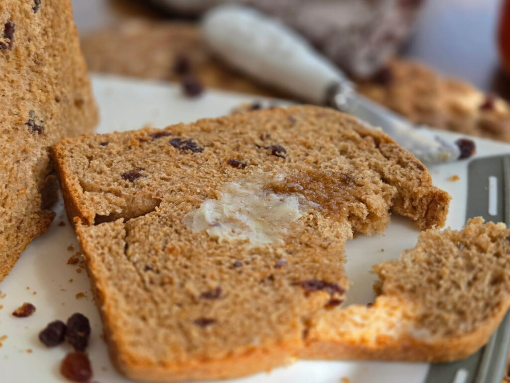 Piece of cinnamon raisin bread with melted butter and honey and corner broken off to show crumb