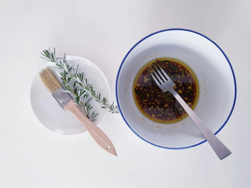 oil and vinegar in bowl with fork next to plate of fresh rosemary